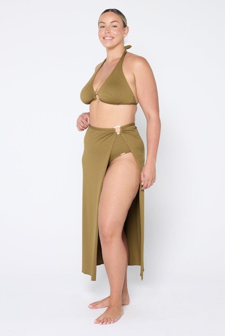 Woman wearing an olive green bikini and matching sarong on a white background