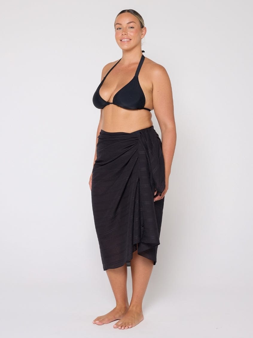 Woman wearing a black bikini and black sarong against a white background