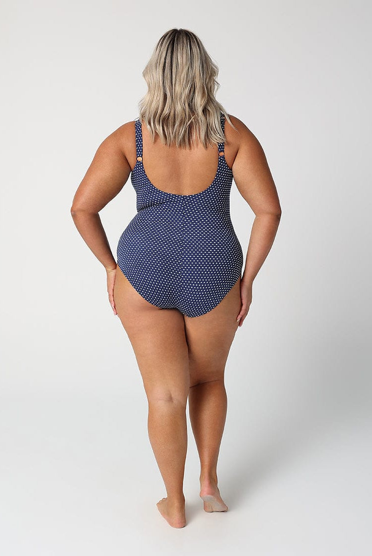 Person wearing a navy polka dot swimsuit on a white background