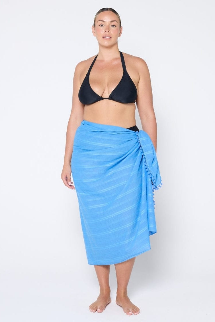 Woman wearing a black bikini top and blue sarong on a white background