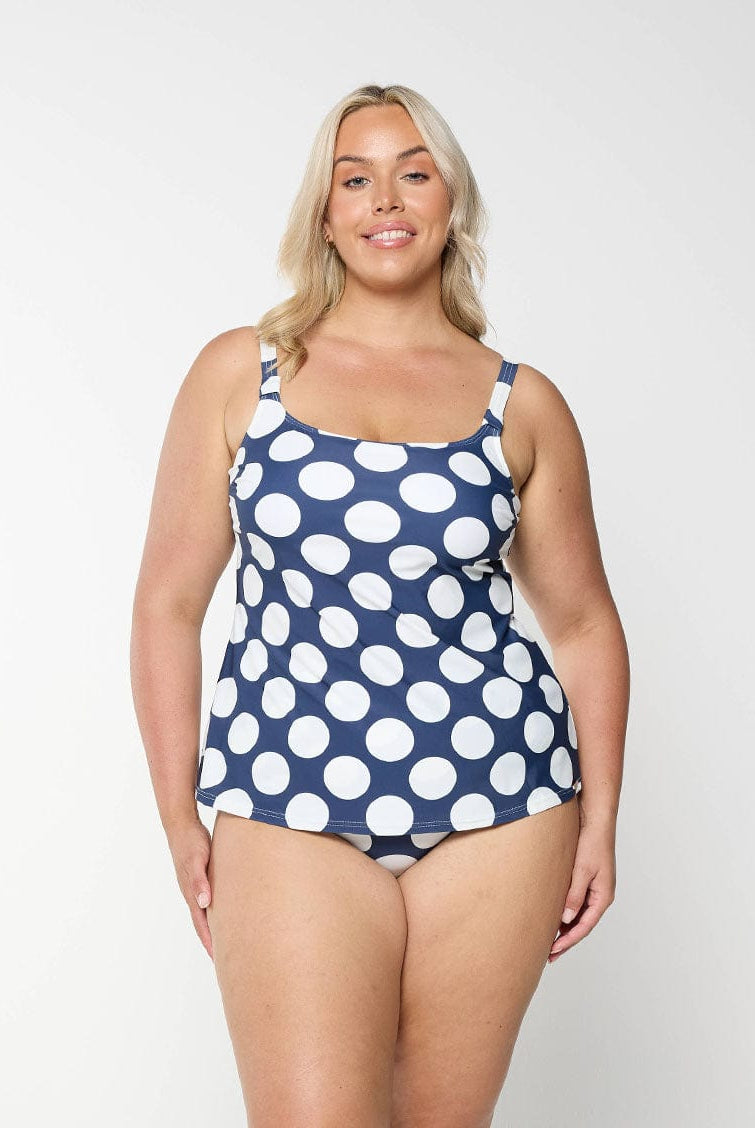 Blonde model shows the front of a flattering scoop neck tankini top with a navy and white polkadot pattern