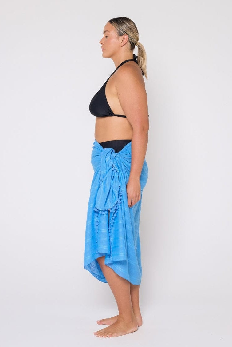 Woman wearing a black bikini top and blue sarong against a white background
