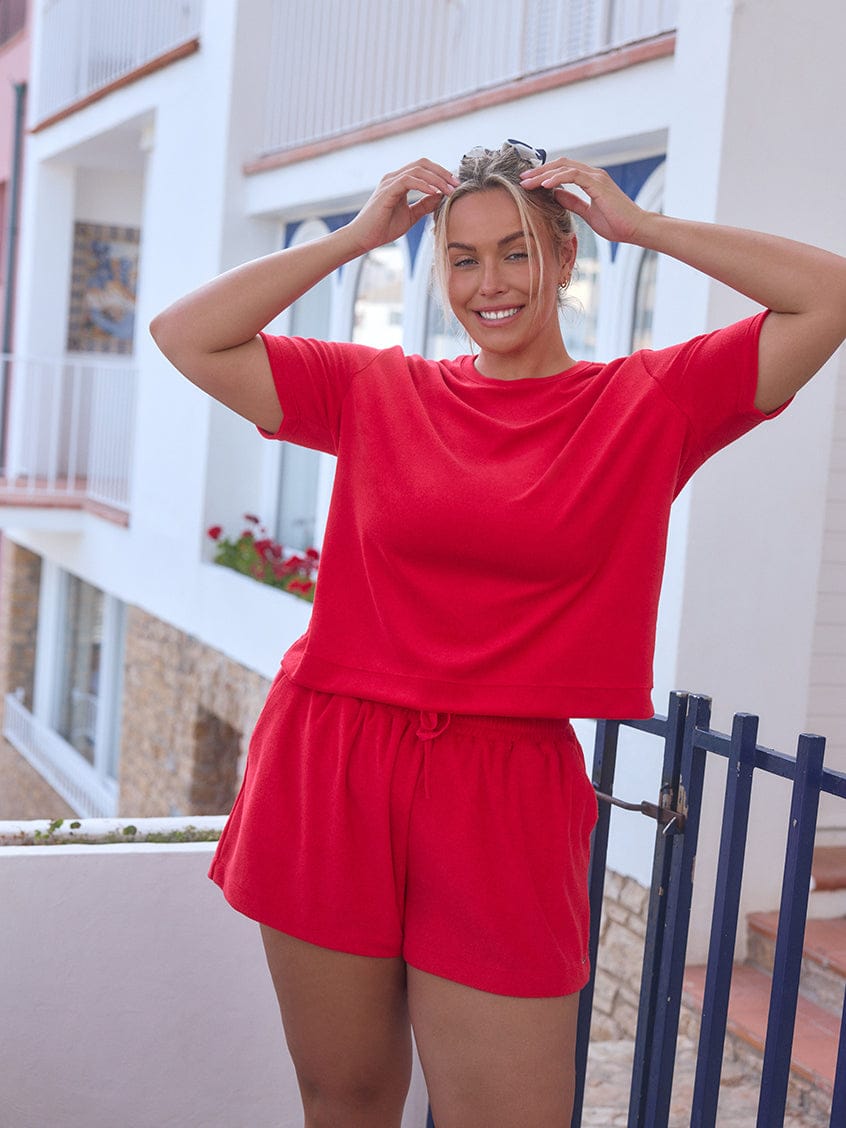 Woman in a red outfit standing on a balcony with a building in the background