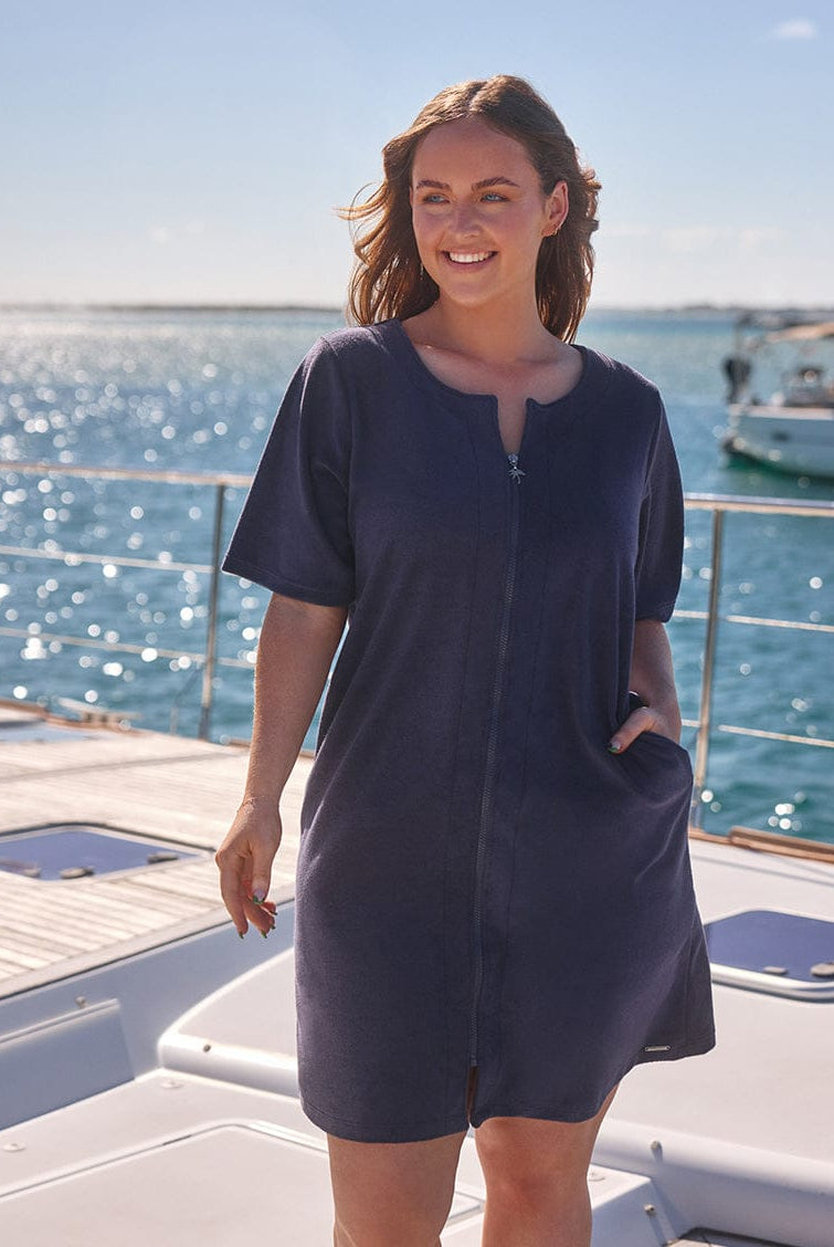 Woman in a navy blue dress standing on a boat with water and sky in the background