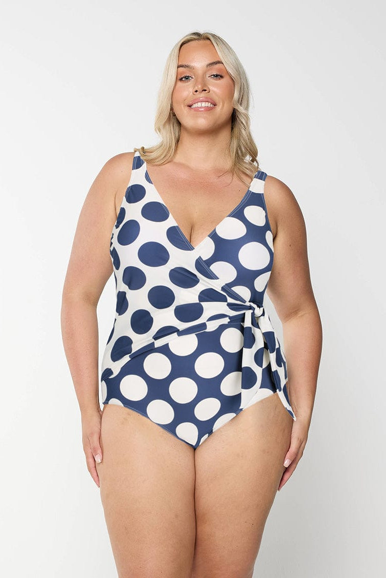 Woman wearing a blue and white polka dot swimsuit on a plain background