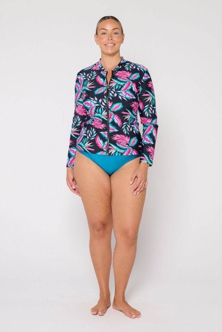 Woman wearing a colorful tropical print shirt and blue swimsuit on a white background
