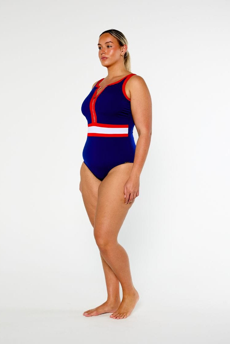 A woman modeling a one-piece swimsuit with a royal blue base and red and white stripe details, standing against a plain white studio background.