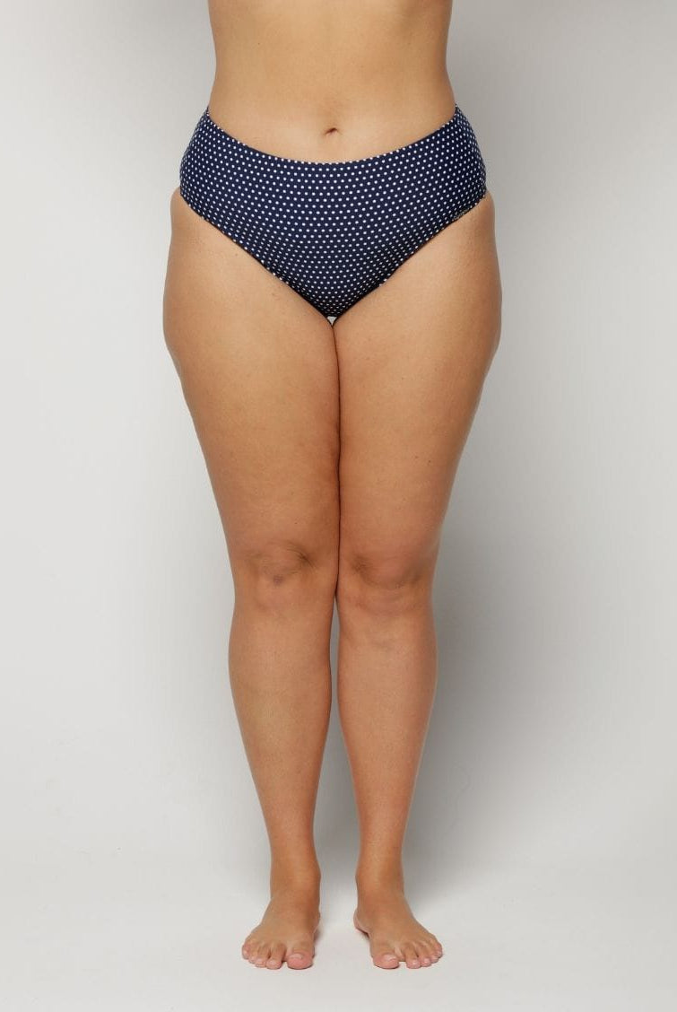 Woman wearing navy polka dot high-waisted bikini bottoms on a light gray background