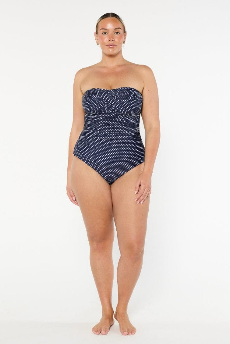Woman wearing a strapless navy swimsuit with white polka dots on a white background