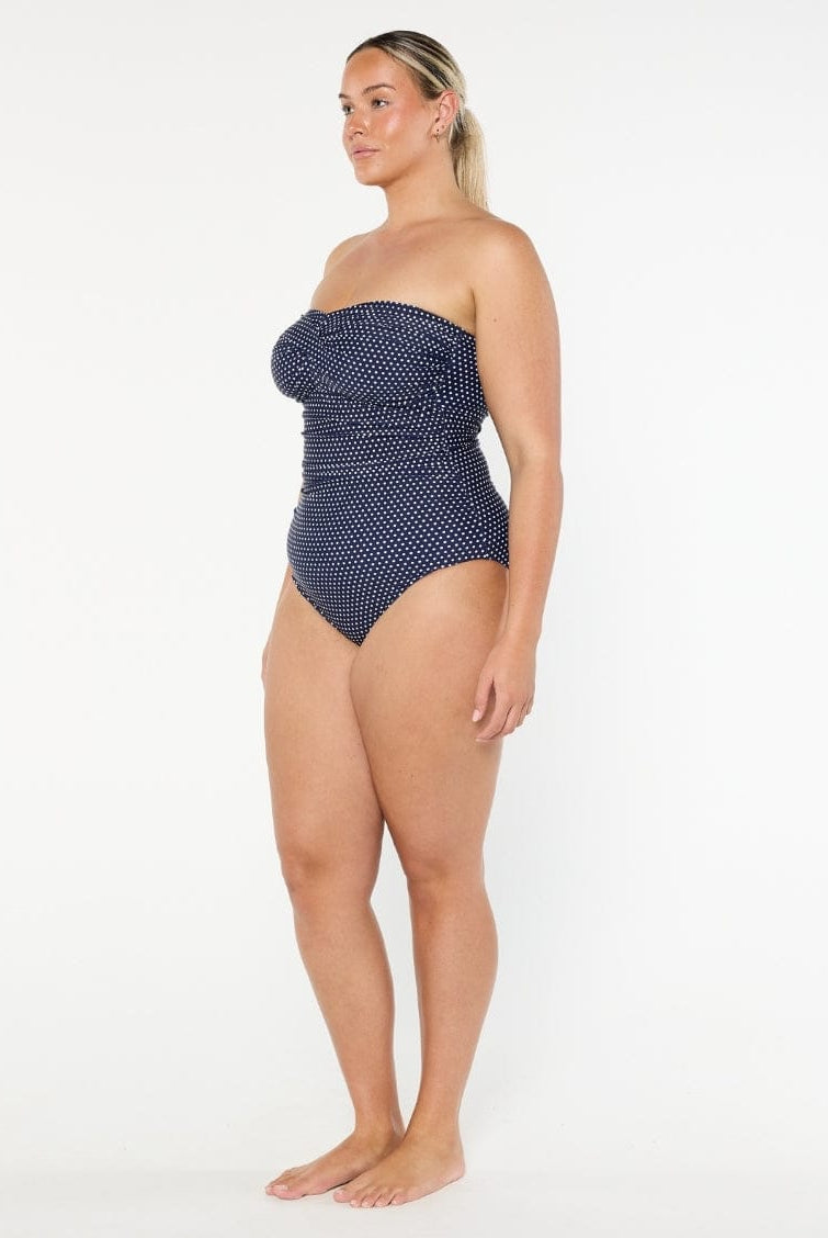 Woman wearing a navy polka dot strapless swimsuit on a white background