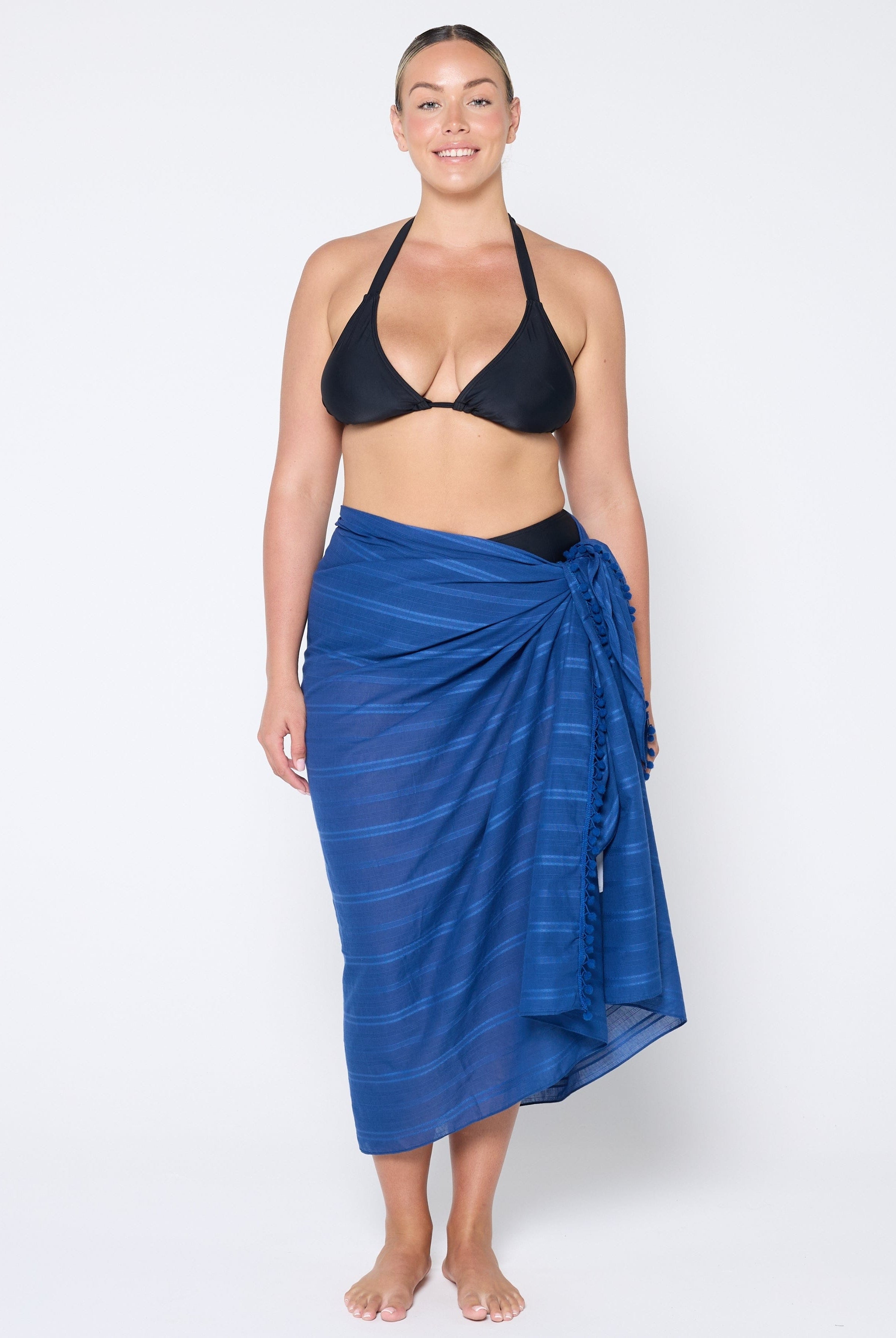 Woman wearing a black bikini top and blue striped sarong on a white background