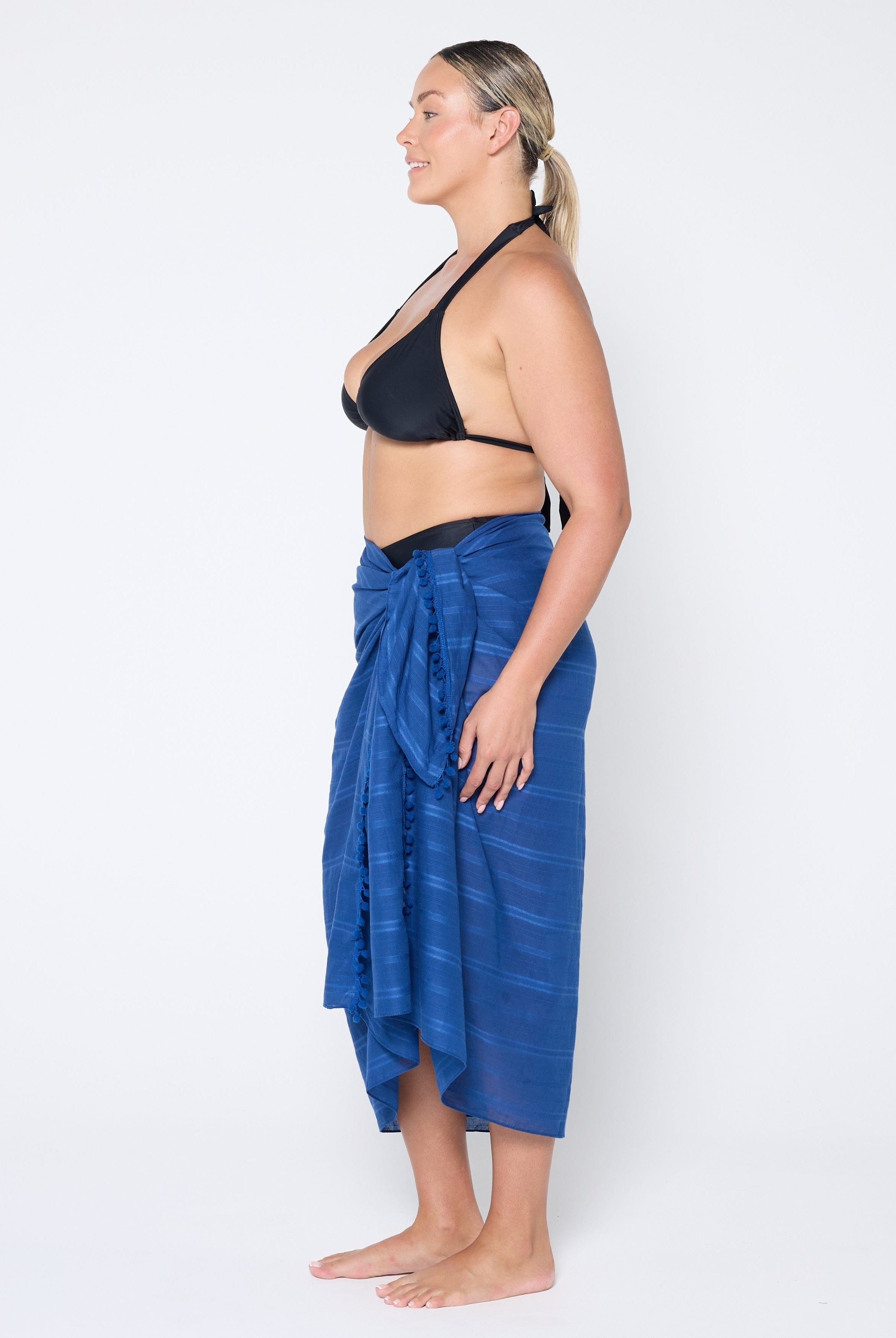 Woman wearing a blue sarong and black bikini top on a white background