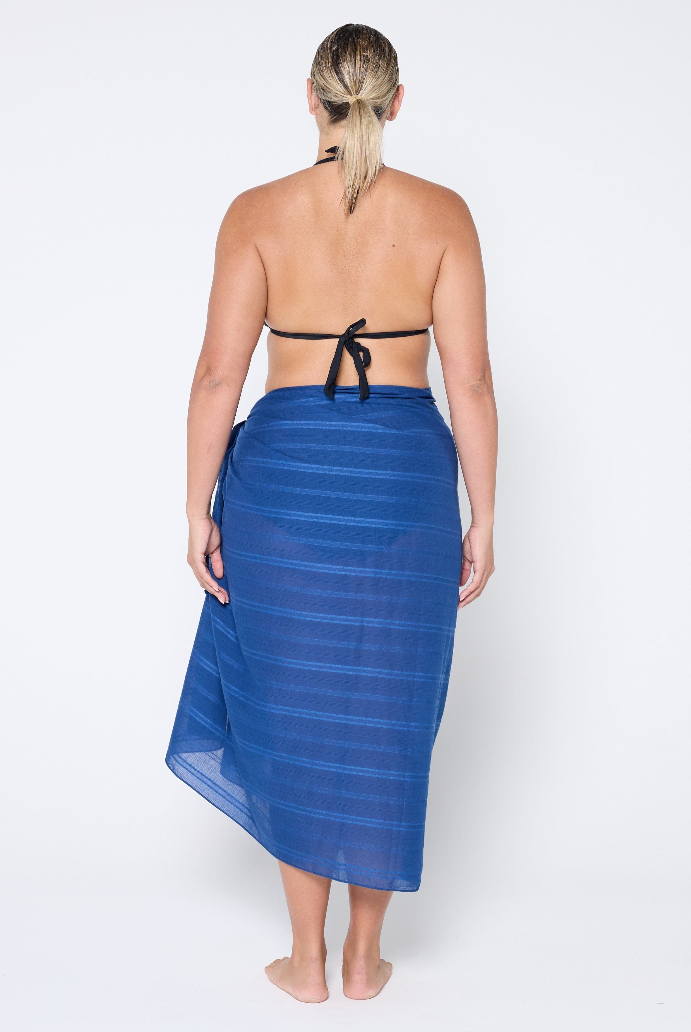 back of model standing in front of a white wall wearing a navy blue sarong