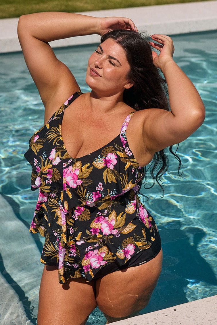 Brunette model wears chlorine resistant pink and gold floral tankini top with ruffles in the pool