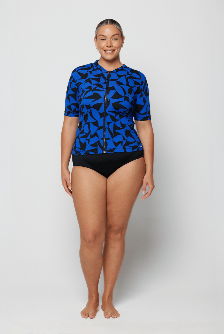 Woman wearing a blue patterned rash guard and black shorts on a white background