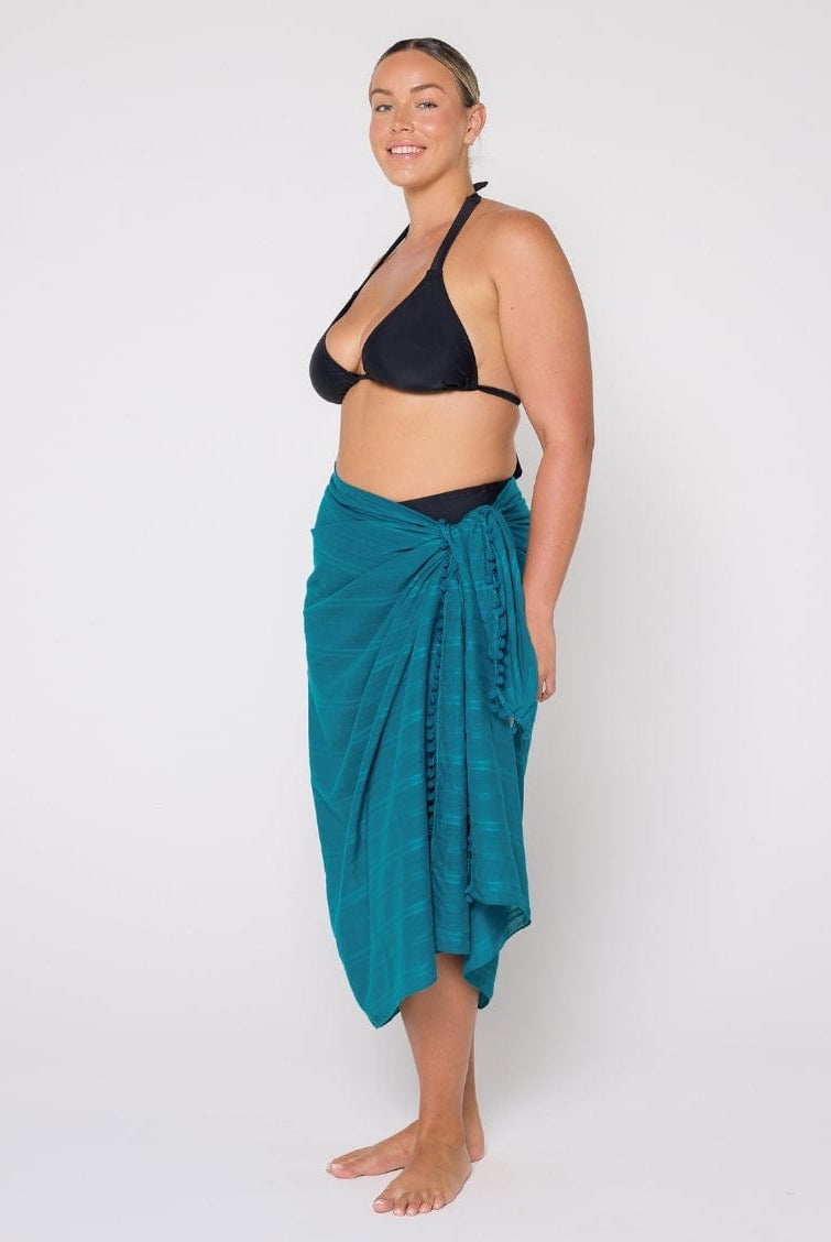 Woman wearing a black bikini and teal sarong on a white background