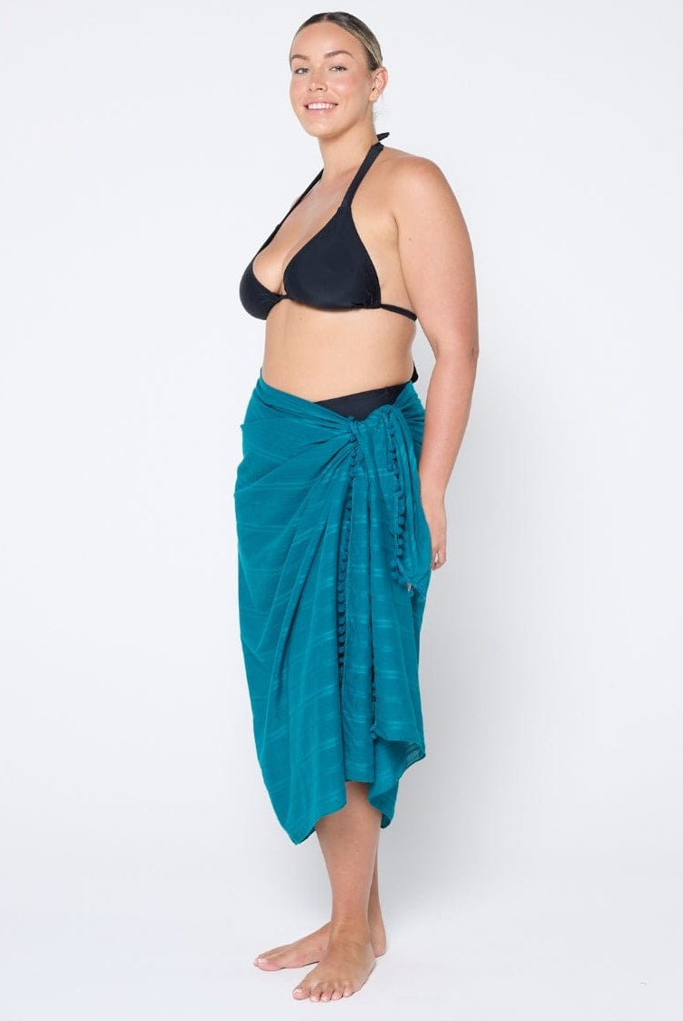 Woman wearing a black bikini top and teal sarong on a white background
