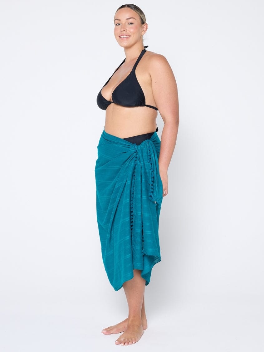 Woman wearing a black bikini top and teal sarong on a white background