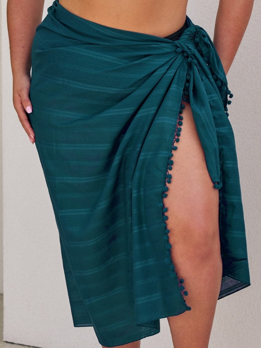Teal sarong with pom-pom details on a plain background