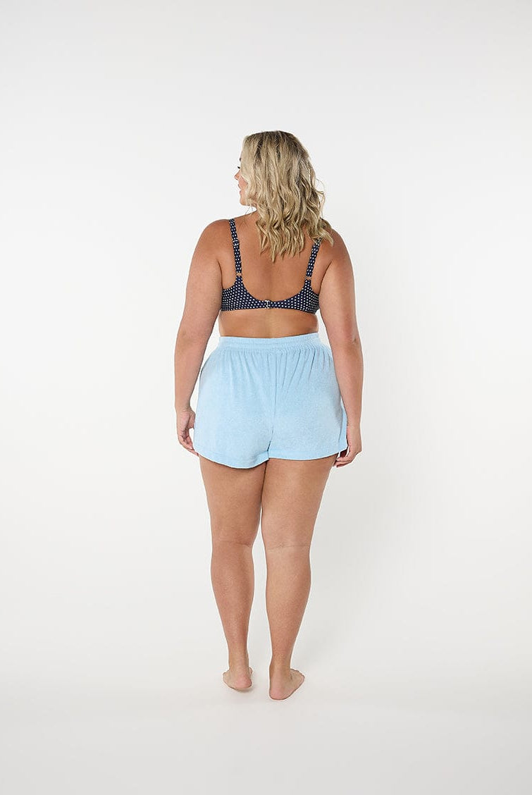 Woman wearing a navy bra and light blue shorts on a white background