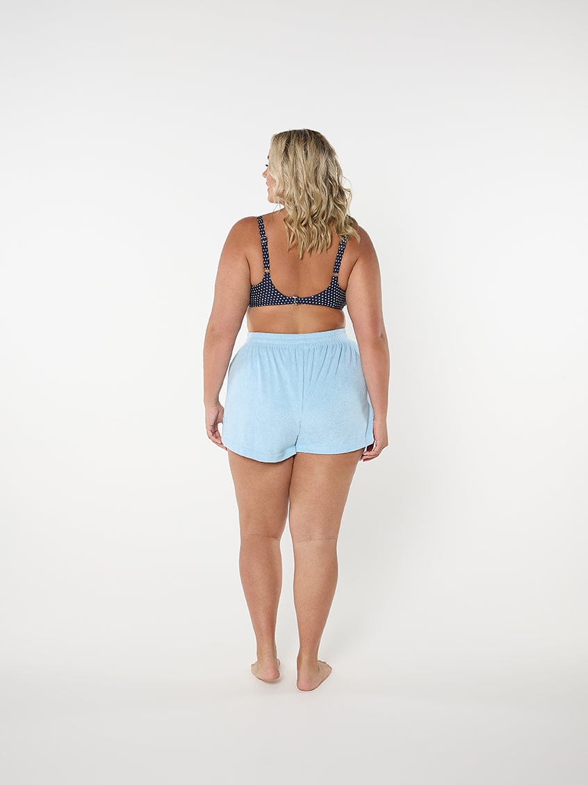 Woman wearing a navy bra and light blue shorts on a white background