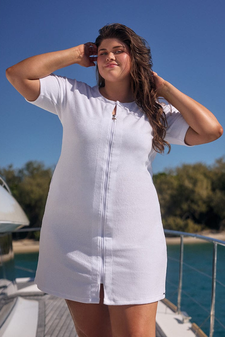 Woman in a white dress standing on a boat with a clear blue sky and trees in the background