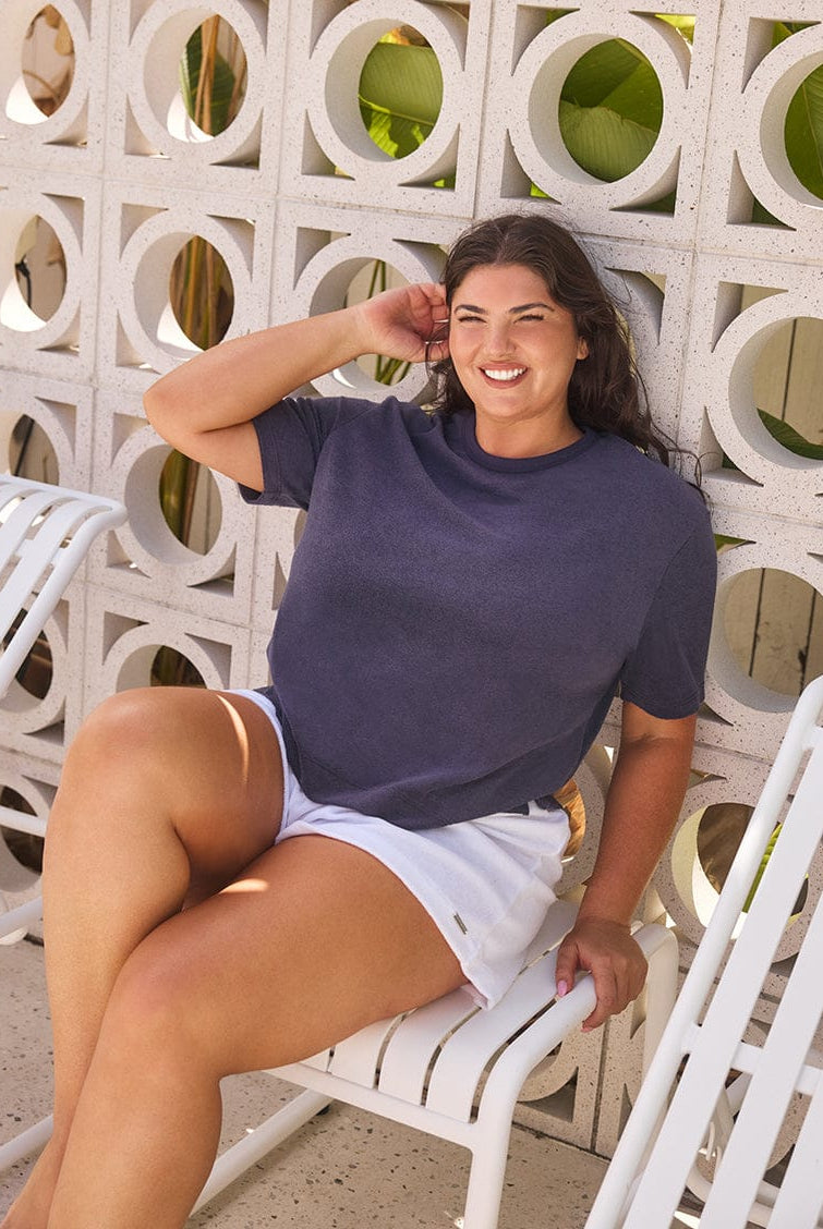 Woman sitting on a white chair against a decorative stone wall.
