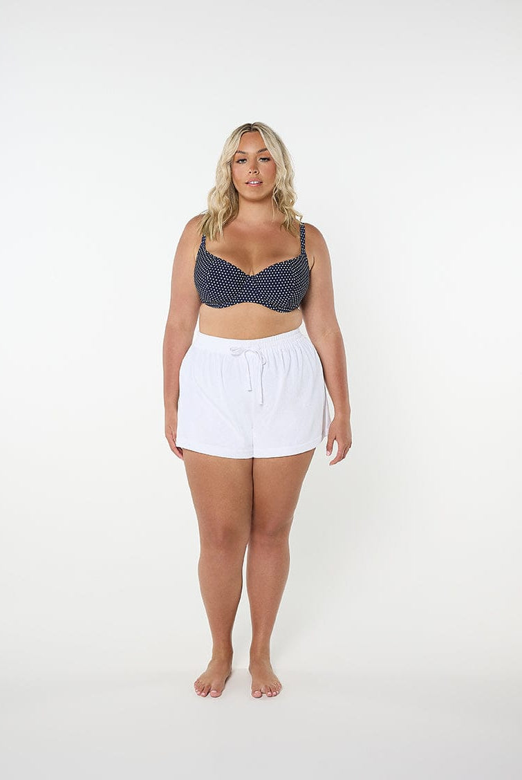Woman wearing a navy patterned top and white shorts on a white background
