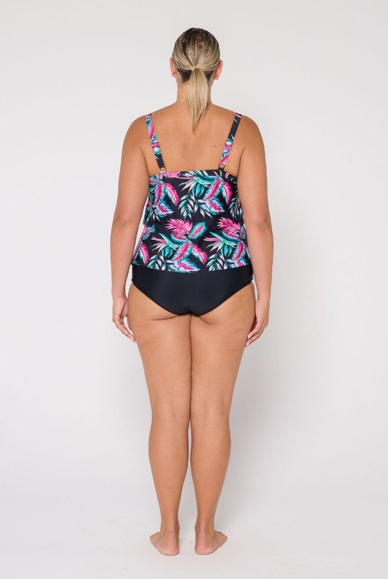 A woman viewed from the back wearing a 3 tier tankini with a black base and a colorful tropical leaf pattern in pink, teal, and green, paired with solid black bottoms, against a plain white studio background.