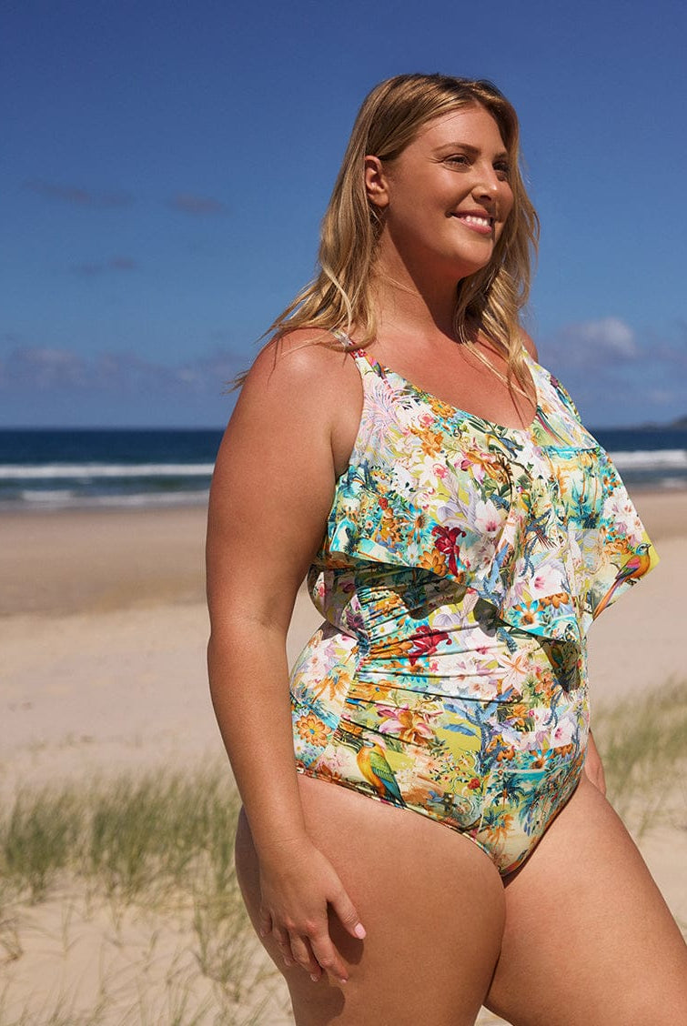 Woman in a floral swimsuit standing on a beach with ocean and sky in the background