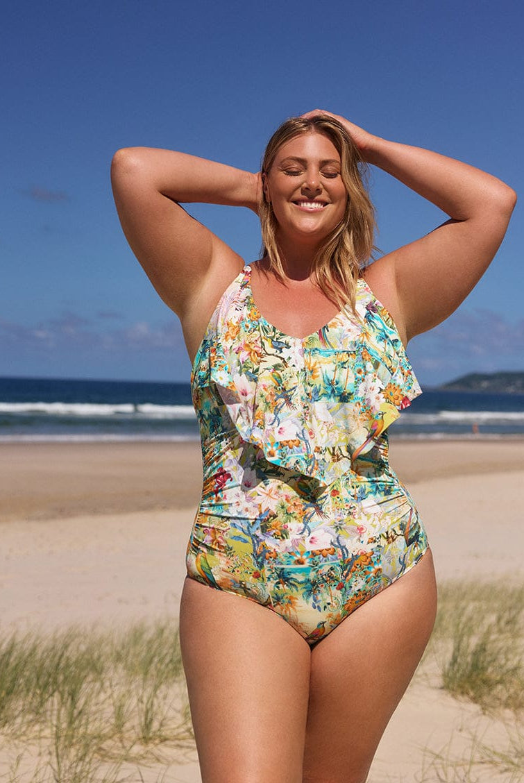 Woman in a floral swimsuit standing on a beach with ocean and sky in the background