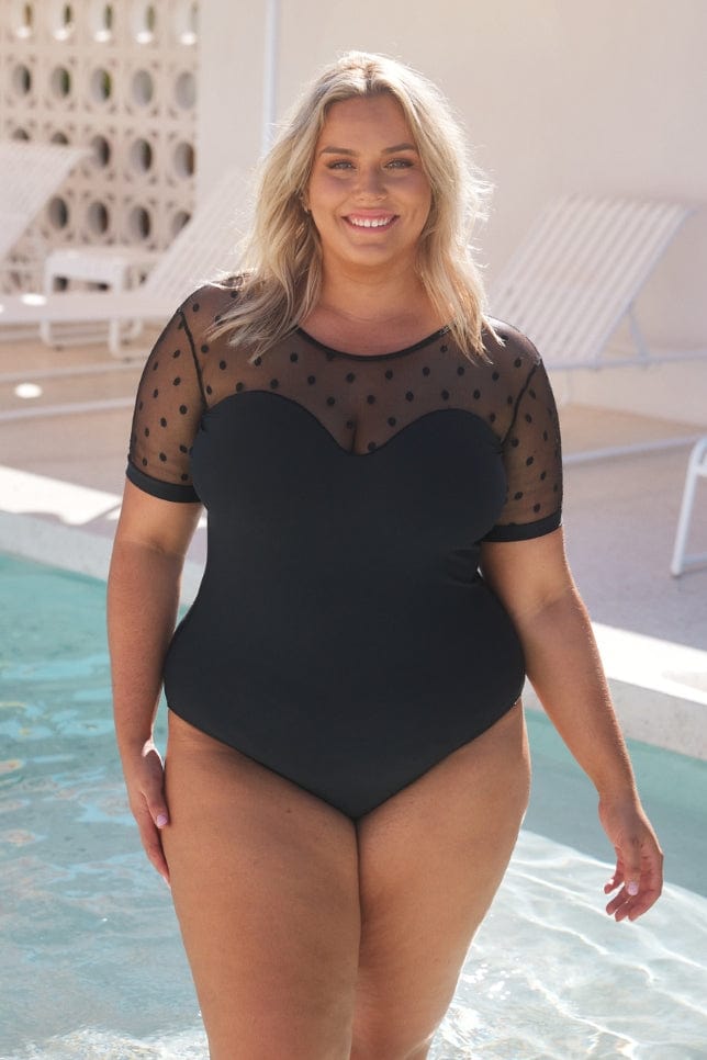 blonde model wearing the high neck mesh polkadot one piece with short sleeves and sweetheart detail neckline