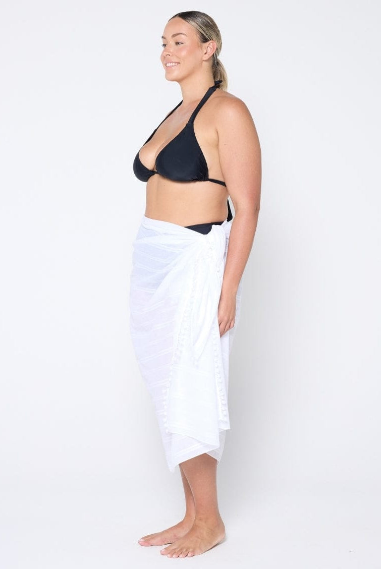 model wearing a white sarong with a black bikini top on a white wall