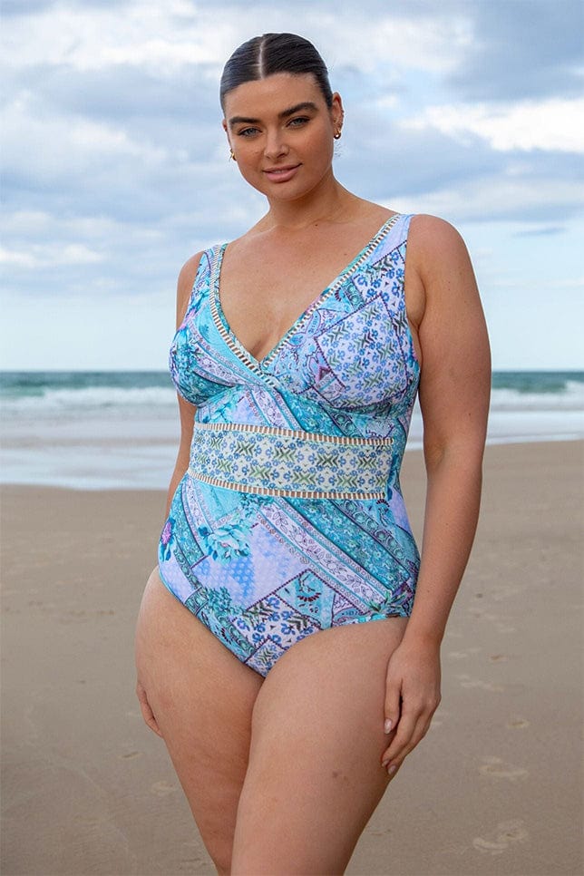 brunette model wearing a v neck one piece swimsuit in aqua blue patchwork print