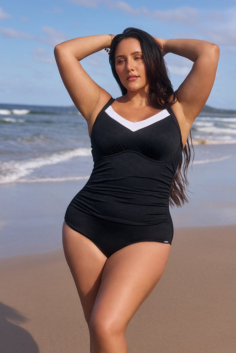 Woman wearing a black swimsuit with white accents on a beach