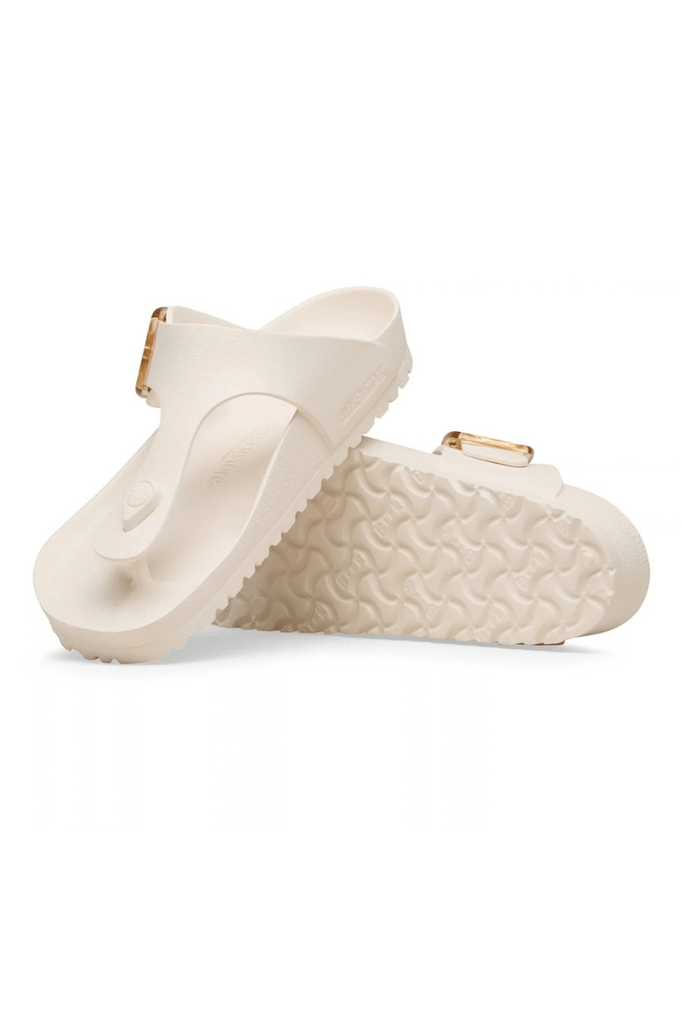 A pair of off-white double-strap slide sandals with textured soles and small gold-tone buckle details, shown on a clean white background.