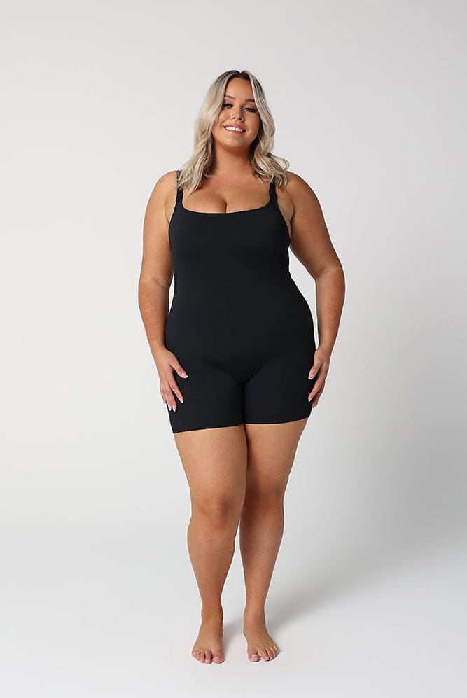 model wearing black boyleg one piece in front of a white wall