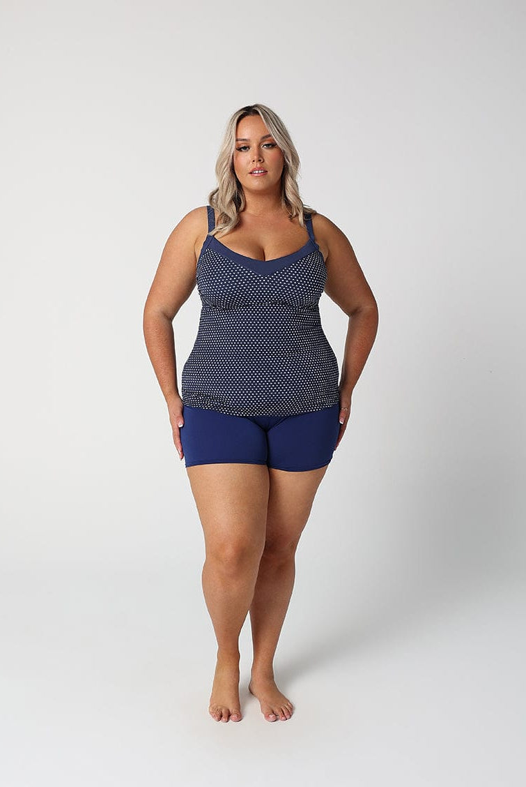 Woman wearing a navy patterned tank top and blue shorts on a white background