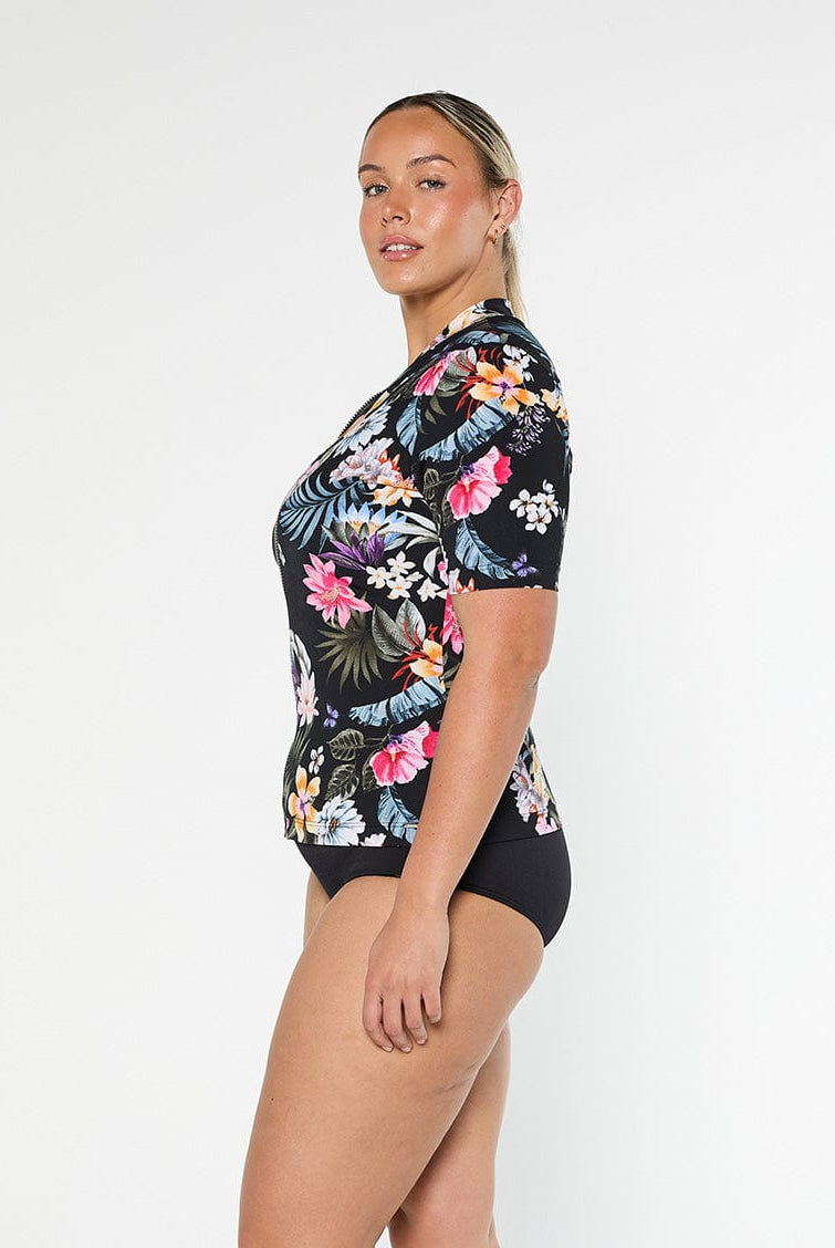 Blonde model shows the side of pool proof rash vest with short sleeve in a black based floral print