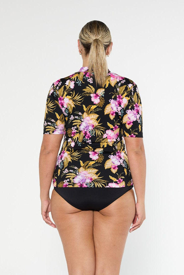 Blonde model shows the full coverage back of tropical floral short sleeve rash vest