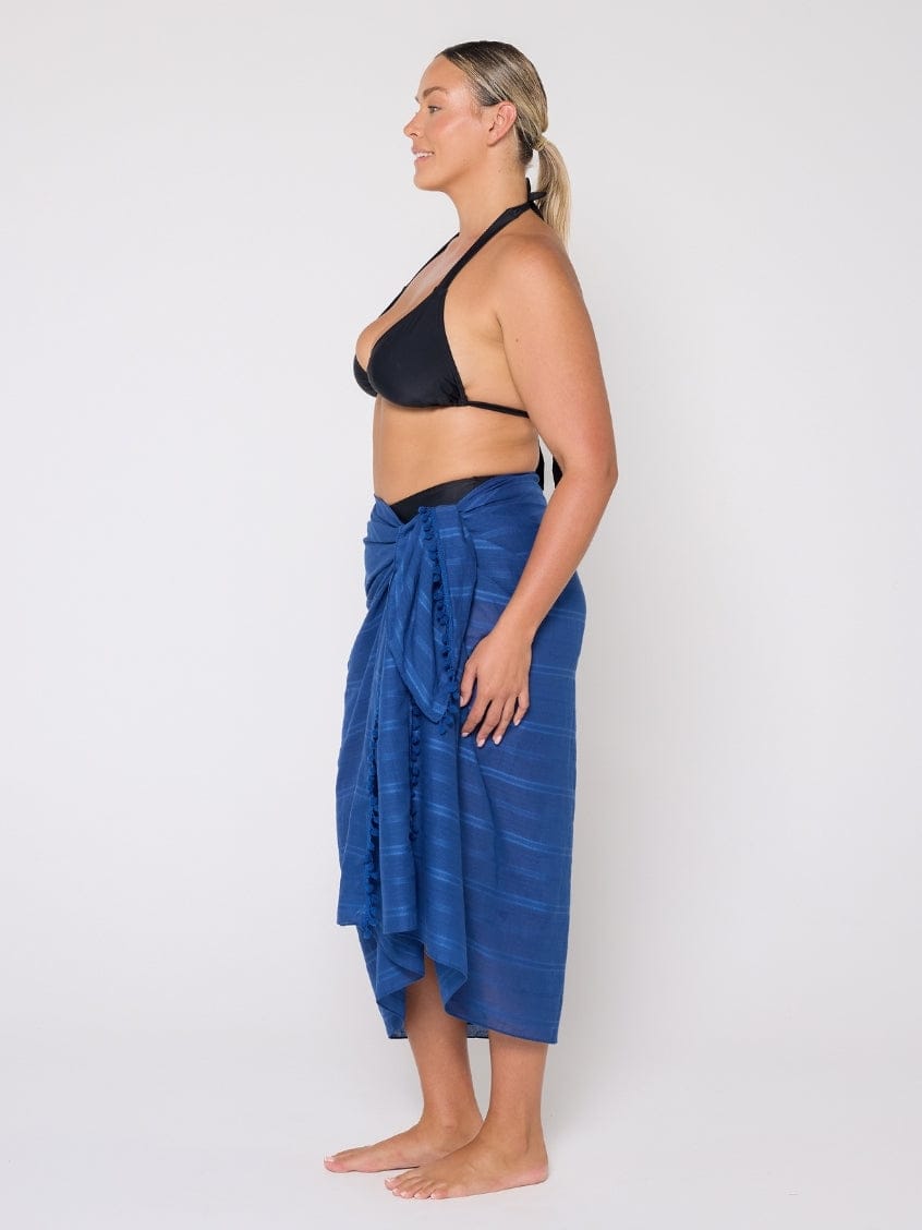 Woman wearing a black bikini top and blue sarong against a white background