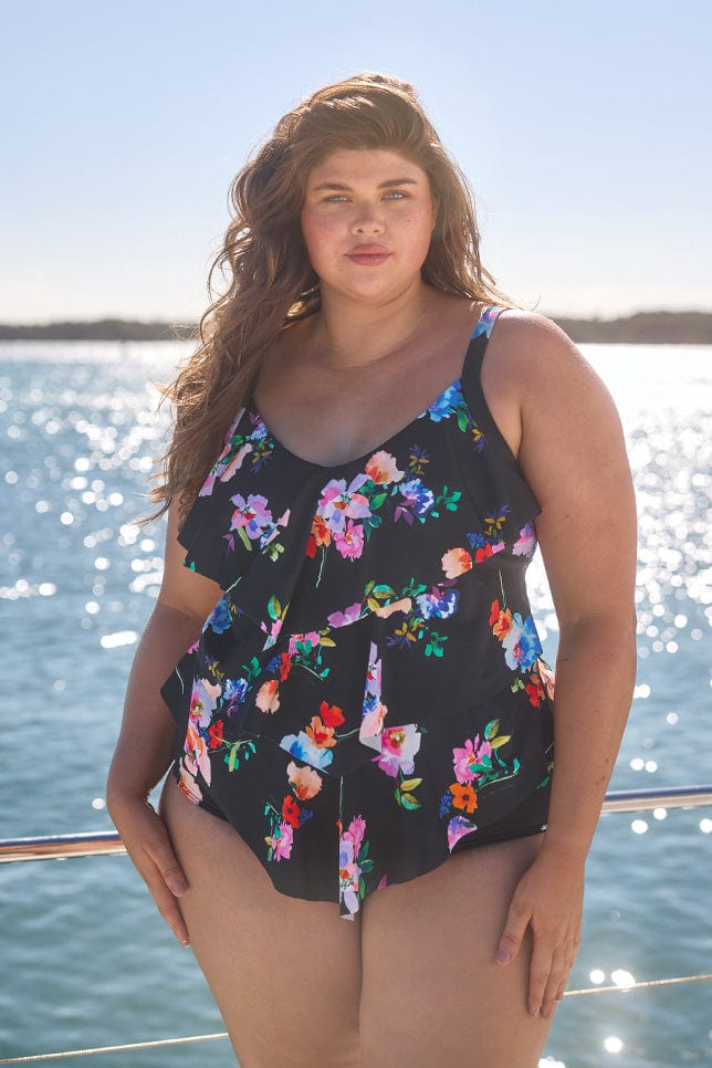 Model wearing black with bright florals 3 tier tankini and matching pant on boat
