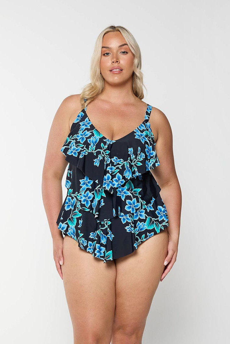 Blonde model shows front of blue floral swimsuit top with 3 ruffles