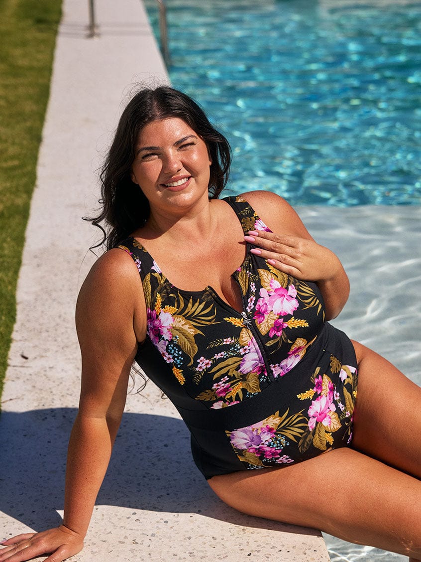 Brunette model wears pink and gold floral chlorine resistant floral zip front one piece to the pool