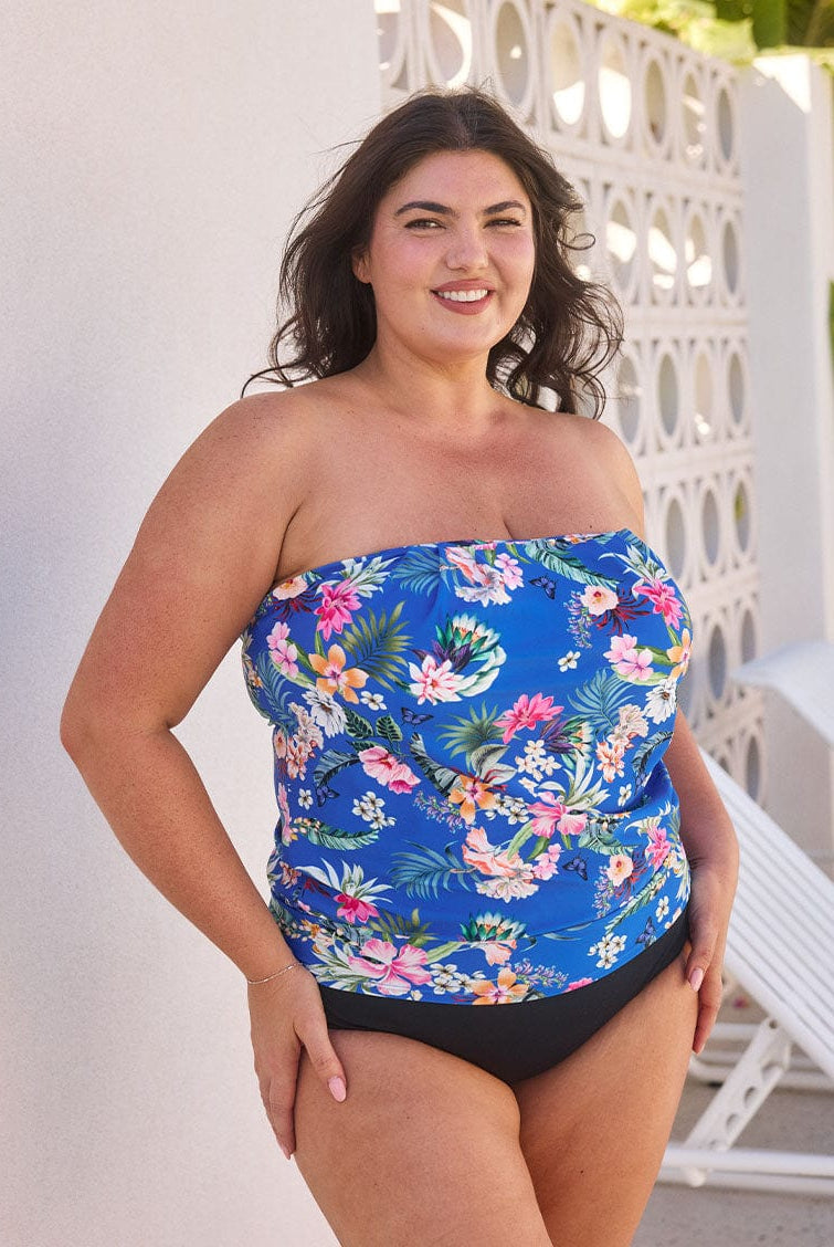 Brunette model wears bandeau tankini top with the straps removed in a vibrant blue floral print