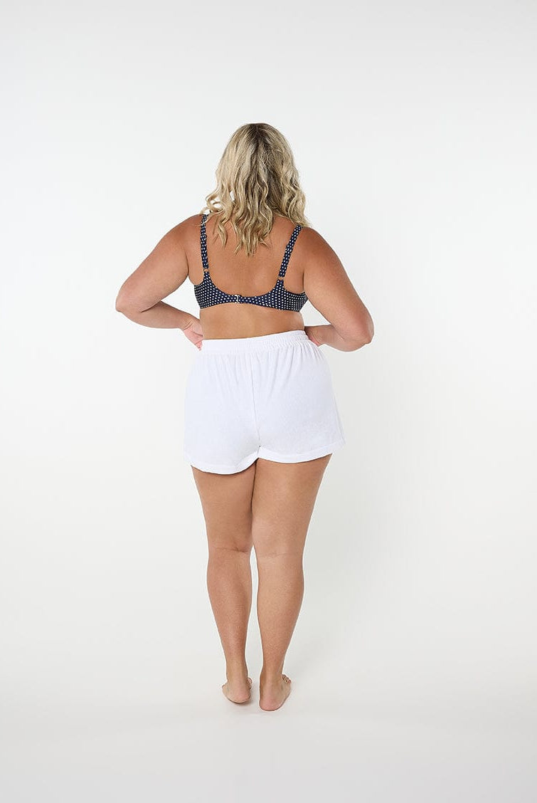 Woman wearing a polka dot bralette and white shorts on a white background