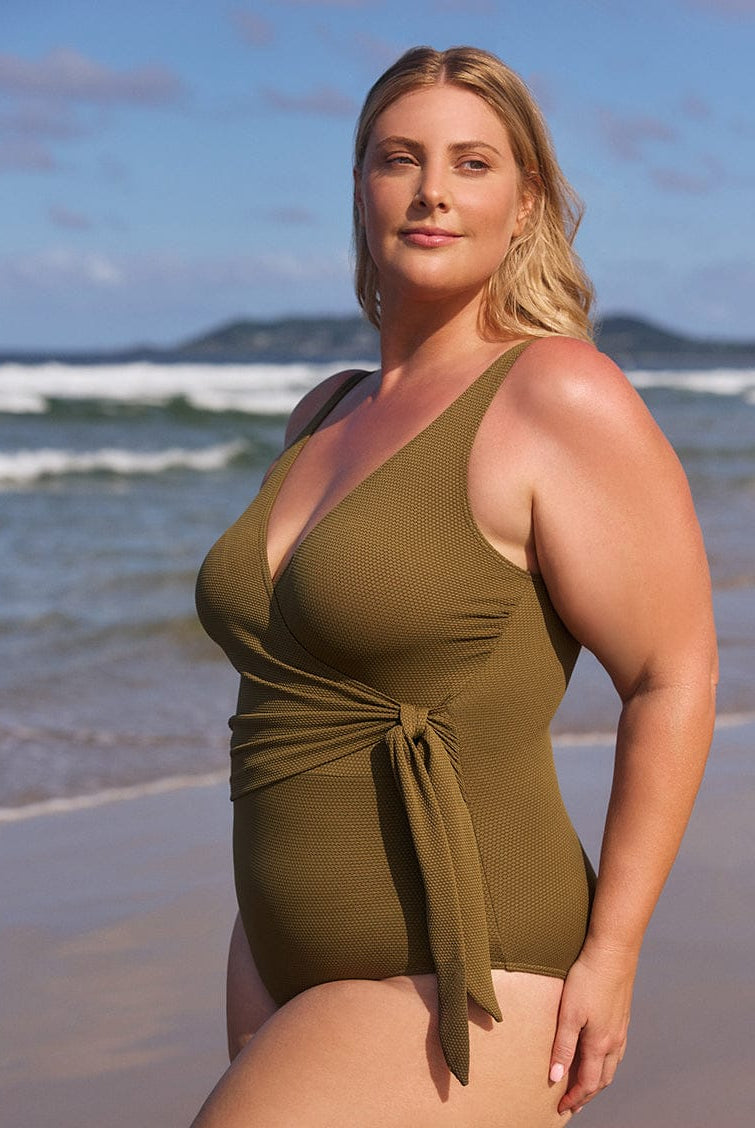 Woman wearing a green swimsuit on a beach with ocean and sky in the background
