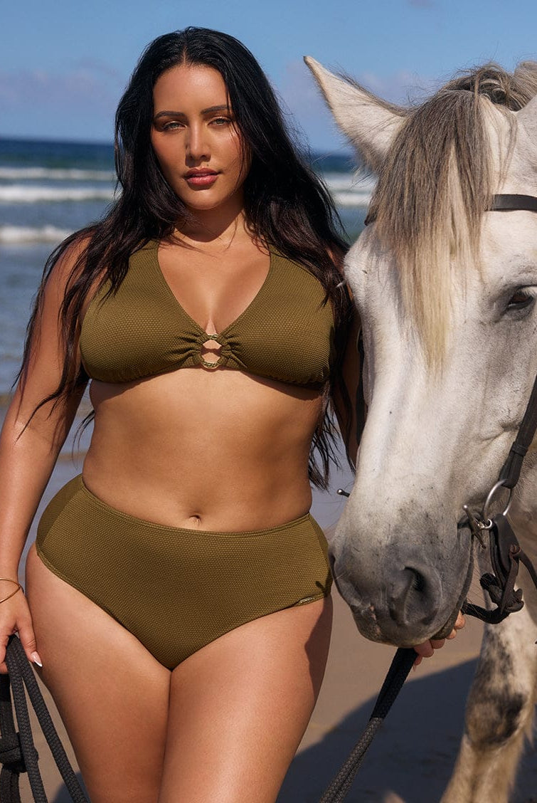 Woman in a green bikini standing next to a horse on a beach