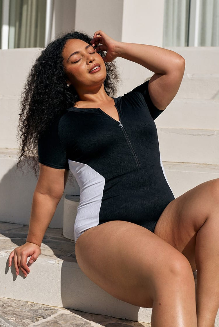 Model sitting down wearing a chlorine resistant short sleeve one piece with textured print