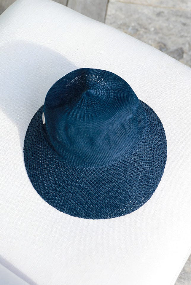 foldable navy blue straw beach hat laying on a white arm chair by the pool